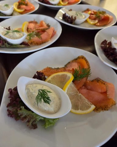 Vorspeise mit Räucherlachs, Zitronenscheiben, Salat und cremiger Sauce.
